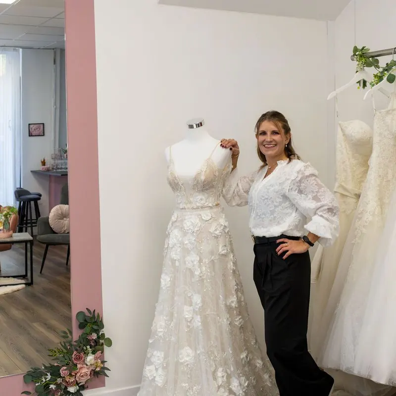 Barbara lacht neben einem Brautkleid vor dem großen Spiegel