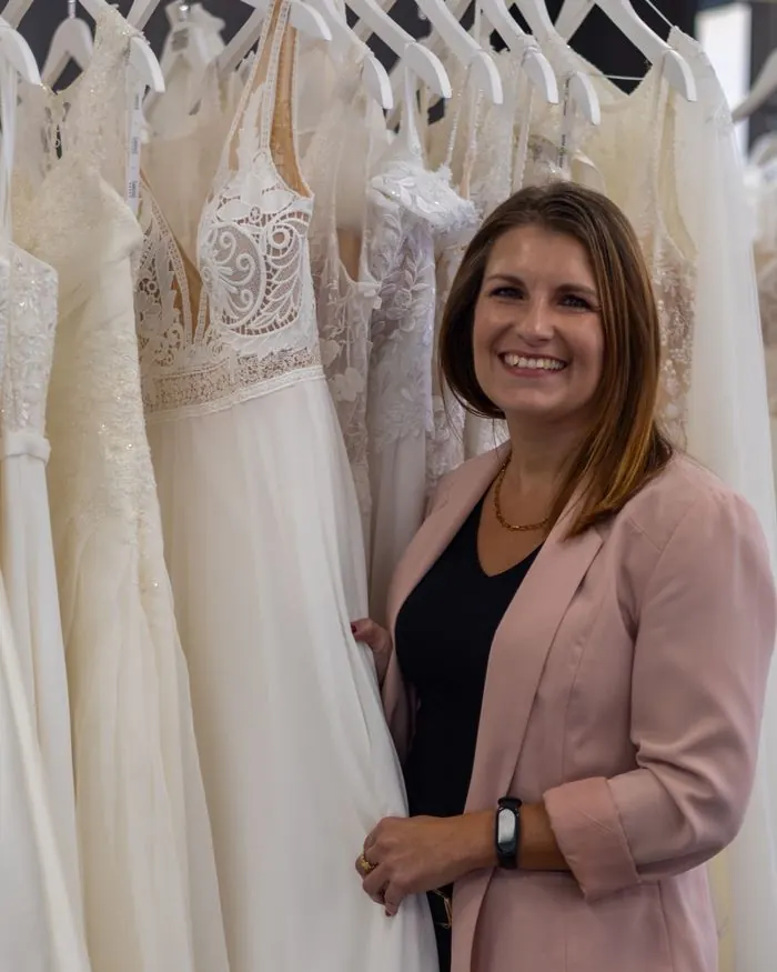 Barbara präsentiert lächelnd ein Brautkleid an der Kleiderstange
