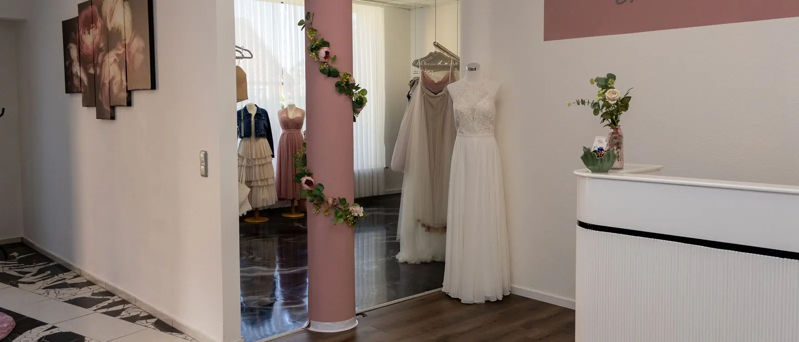 Eingangsbereich von emella mit Theke, rosa Säule und Brautkleidern