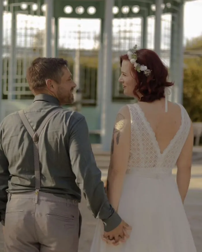 Braut im Spitzenkleid mit V-Rücken, Hand in Hand mit ihrem Mann